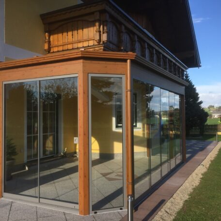 Wintergarten mit Glasfront und Holzrahmen an Einfamilienhaus im Grünen bei Sonnenschein. HANSEL.kraus metalltechnik gmbh