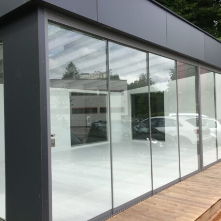 Modernes Glashaus mit großflächigen Fenstern und reflektierenden Oberflächen auf Holzterrasse. HANSEL.kraus metalltechnik gmbh