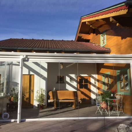Ein helles Wintergartenhaus mit Holzelementen, Glasfront und Terrassenmöbeln bei sonnigem Wetter. HANSEL.kraus metalltechnik gmbh