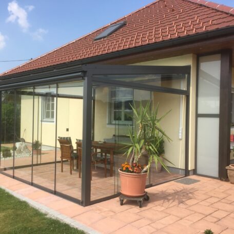 Wintergarten mit Glaswänden und Terrassenmöbeln an modernem Einfamilienhaus, sonniger Gartenbereich. HANSEL.kraus metalltechnik gmbh
