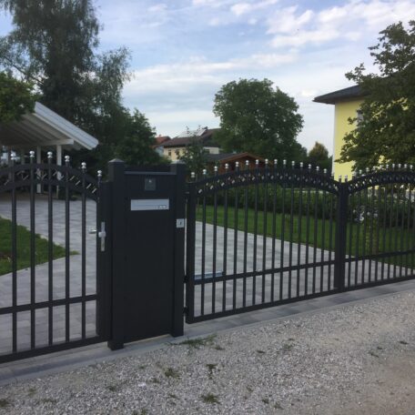 Schwarzes Einfahrtstor aus Metall mit integriertem Briefkasten vor Einfamilienhaus und gepflegtem Garten. HANSEL.kraus metalltechnik gmbh