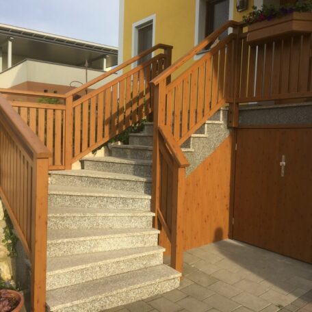 Steintreppe mit braunem Holzgeländer führt zu gelbem Haus und Abstellraum im Außenbereich. de HANSEL.kraus metalltechnik gmbh