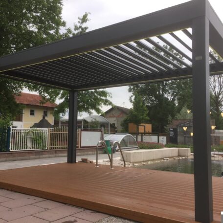 Moderne Terrassenüberdachung mit Lamellendach neben Pool, umgeben von Garten und Häusern. HANSEL.kraus metalltechnik gmbh