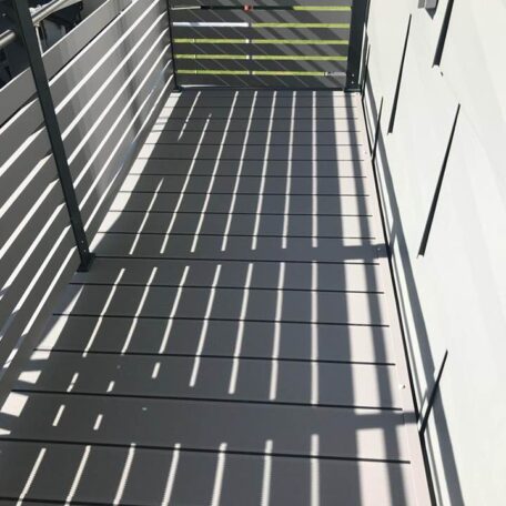Schatten von Metallgeländer fällt auf modernen Balkonboden, Wand rechts, draußen, Tageslicht. HANSEL.kraus metalltechnik gmbh