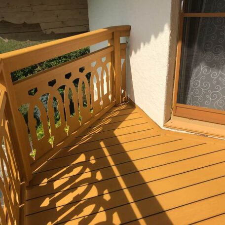 Holzbalkon mit dekorativem Geländer an einem Haus, sonnig, Zugang durch Glastür. HANSEL.kraus metalltechnik gmbh