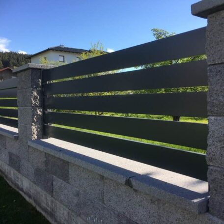 Moderner Gartenzaun aus Metall mit Steinmauer vor einem Haus bei sonnigem Wetter. HANSEL.kraus metalltechnik gmbh