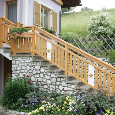 Steintreppe mit Holzgeländer führt an blühenden Gartenpflanzen zu einem Haus mit violetter Fassade. HANSEL.kraus metalltechnik gmbh