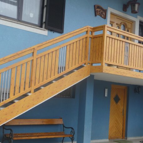 Holztreppe an blauer Hausfassade mit Eingangstür und Sitzbank im Eingangsbereich. HANSEL.kraus metalltechnik gmbh