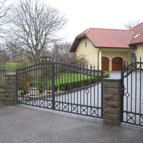 Einfahrtstor aus Metall vor Einfamilienhaus mit Garten und gepflastertem Weg bei bewölktem Wetter. HANSEL.kraus metalltechnik gmbh