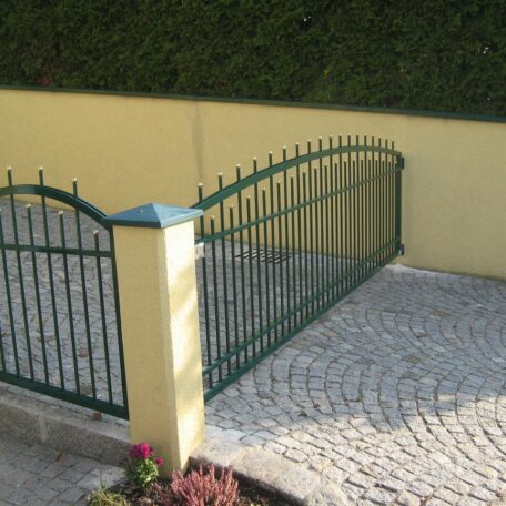 Grünes Metalltor auf gepflasterter Einfahrt vor gelber Mauer, Hecke im Hintergrund. HANSEL.kraus metalltechnik gmbh
