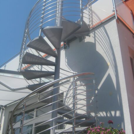 Moderne Wendeltreppe aus Metall an einer weißen Hausfassade bei Sonnenschein. HANSEL.kraus metalltechnik gmbh