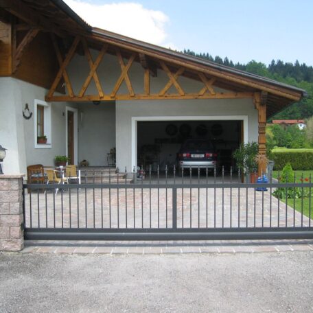 Modernes Einfamilienhaus mit offenem Garagentor und schwarzem Einfahrtstor im Vordergrund. de HANSEL.kraus metalltechnik gmbh