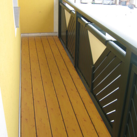 Schmaler Balkon mit gelber Wand und Holz-Optik Bodenbelag, moderne Metallbrüstung. HANSEL.kraus metalltechnik gmbh