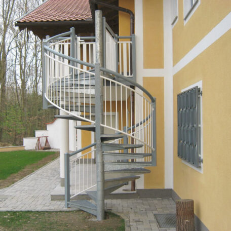 Metallwendeltreppe außen an gelbem Haus mit Garten, Zugang zum Obergeschoss. HANSEL.kraus metalltechnik gmbh