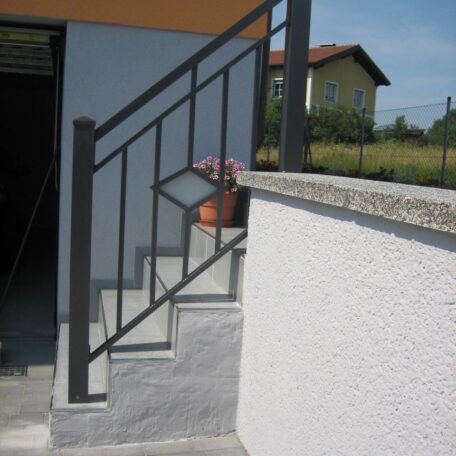 Außentreppe mit Metallgeländer neben weißer Wand, Blumentopf oben auf der Stufe. HANSEL.kraus metalltechnik gmbh