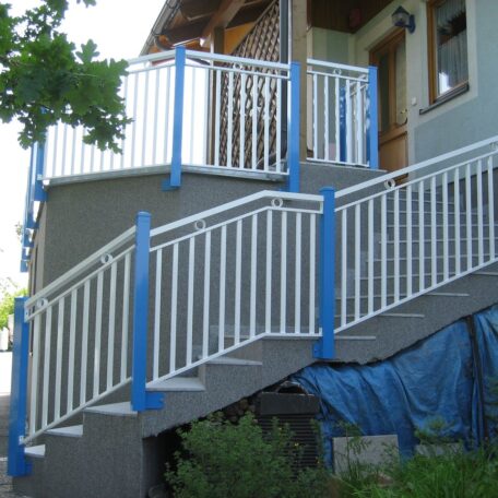 Geländer aus weißem Metall mit blauen Pfosten an einer Außentreppe eines Hauses. HANSEL.kraus metalltechnik gmbh