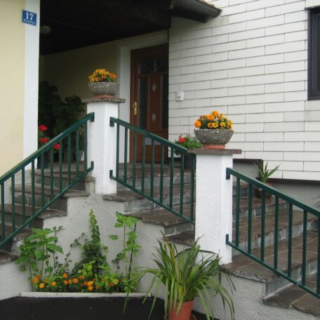 Hauseingang mit Treppe, grünen Geländern und bepflanzten Blumenkübeln vor der Tür. HANSEL.kraus metalltechnik gmbh