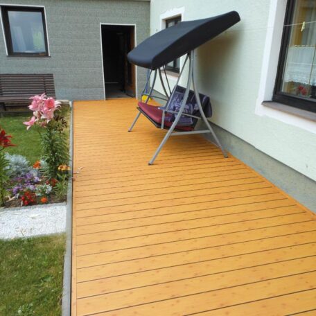 Barrierefreie Holzterrasse mit Gartenbank und Schaukelstuhl an Wohnhaus, Blumenbeet links. HANSEL.kraus metalltechnik gmbh
