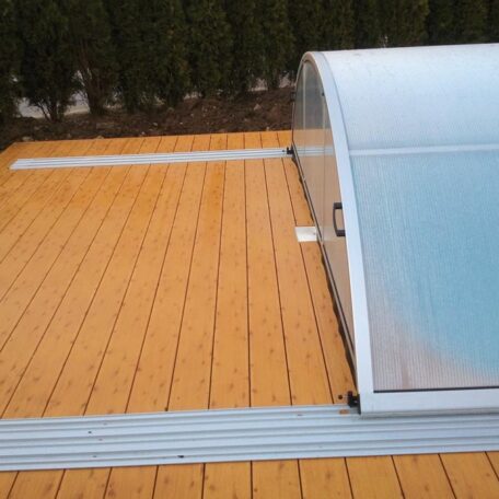 Teilweise geöffnete Poolüberdachung auf einer Terrasse mit Holzbelag bei bewölktem Wetter. HANSEL.kraus metalltechnik gmbh