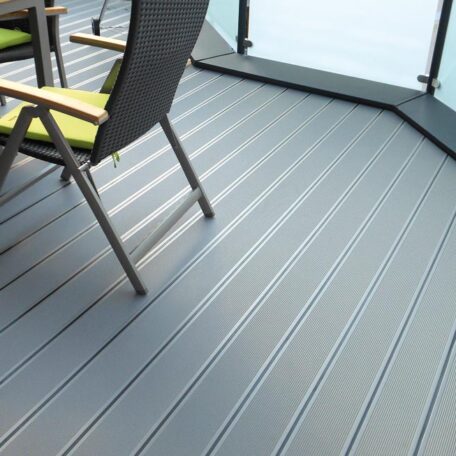 Moderne, graue Terrassendielen mit Tisch und Stühlen auf Balkon, Glasgeländer im Hintergrund. HANSEL.kraus metalltechnik gmbh