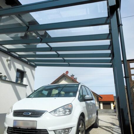 Weißes Auto steht unter modernem Glas-Carport neben Wohnhaus auf sonnigem Grundstück. HANSEL.kraus metalltechnik gmbh