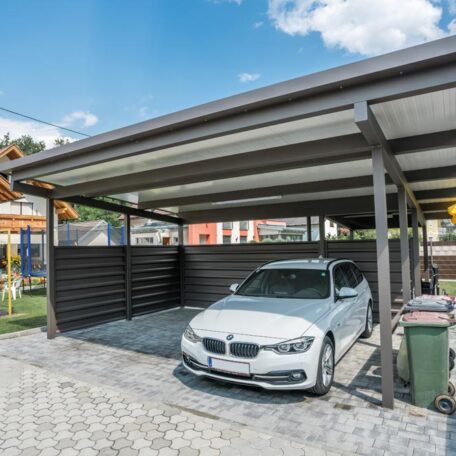Moderner Carport mit geparktem weißen Auto auf gepflastertem Hof bei sonnigem Wetter. HANSEL.kraus metalltechnik gmbh