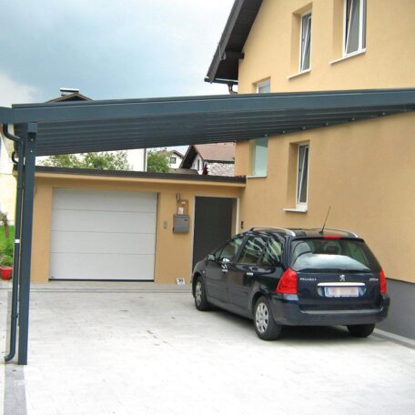 Auto steht unter Carport vor gelbem Einfamilienhaus mit Garage auf gepflasterter Einfahrt. de HANSEL.kraus metalltechnik gmbh