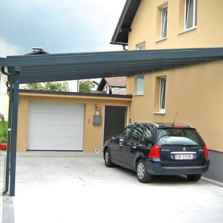 Ein dunkler Pkw steht unter einem Carport neben einem gelben Wohnhaus mit Garage. HANSEL.kraus metalltechnik gmbh