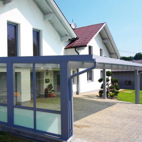 Modernes Einfamilienhaus mit überdachter Terrasse, großer Einfahrt und gepflegtem Garten bei Sonnenschein. HANSEL.kraus metalltechnik gmbh