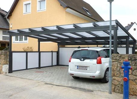 Zweistöckiges Haus mit Carport, darin ein weißes Auto, gepflasterte Einfahrt, moderner Stil. HANSEL.kraus metalltechnik gmbh