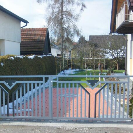 Ein silbernes Metalltor führt zu einem Gartenweg zwischen zwei Wohnhäusern im Vorort. HANSEL.kraus metalltechnik gmbh