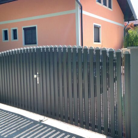 Ein modernes Gartentor aus Metall vor einem orangefarbenen Haus mit mehreren Fenstern. HANSEL.kraus metalltechnik gmbh