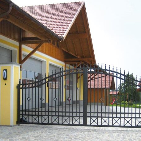Einfahrtstor aus Metall vor modernem Haus mit gelber Säule und Satteldach. HANSEL.kraus metalltechnik gmbh