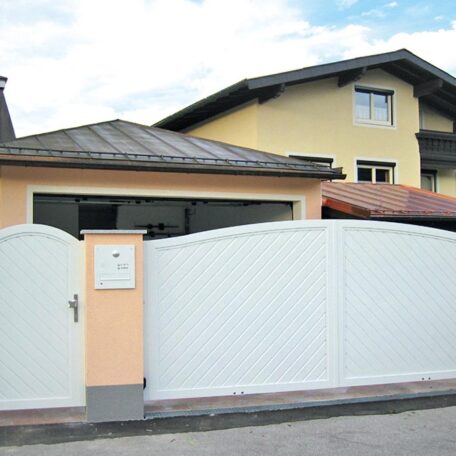 Weißer Gartenzaun mit integriertem Tor vor gelbem Wohnhaus unter blauem Himmel. HANSEL.kraus metalltechnik gmbh