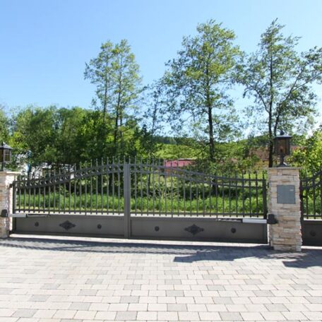 Eisernes Tor mit Natursteinsäulen, dahinter grüne Bäume und blauer Himmel. HANSEL.kraus metalltechnik gmbh