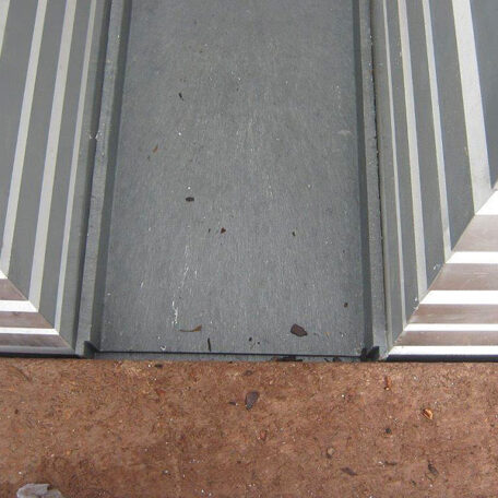 Graue Metalltürschwelle mit Rillen, angrenzend an braunen Bodenbelag, aus Vogelperspektive. HANSEL.kraus metalltechnik gmbh