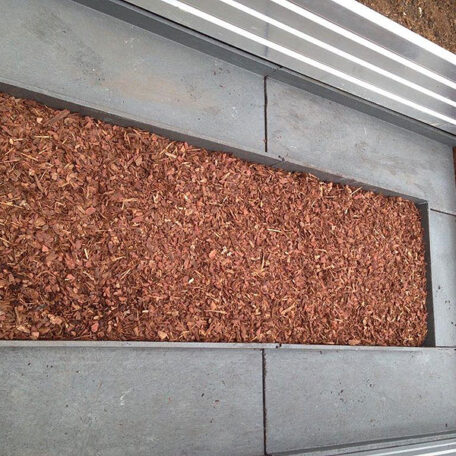 Metallrahmen mit Rindenmulch-Füllung, umgeben von grauen Betonplatten auf Bodenfläche. HANSEL.kraus metalltechnik gmbh
