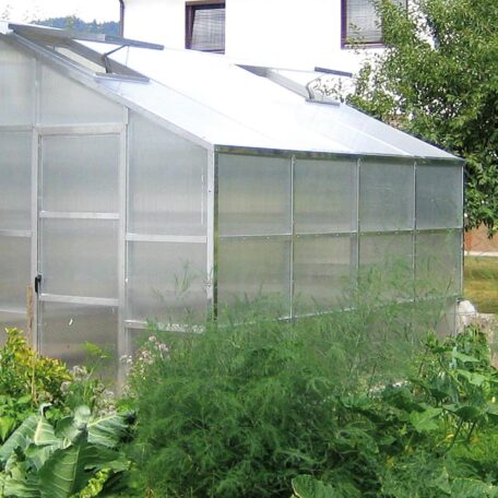 Ein großes Gewächshaus steht im Garten vor einem Wohnhaus, umgeben von grünen Pflanzen. HANSEL.kraus metalltechnik gmbh