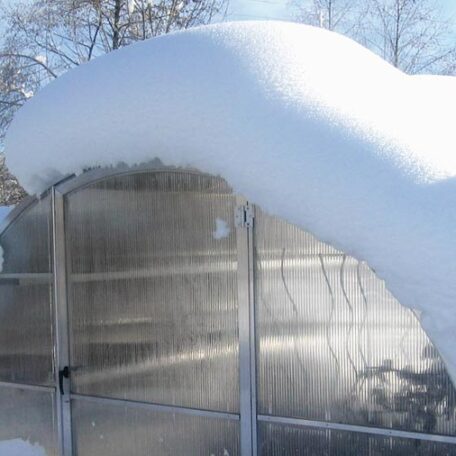 Ein Gewächshaus mit dicker Schneeschicht auf dem Dach, verschneite Winterlandschaft. HANSEL.kraus metalltechnik gmbh