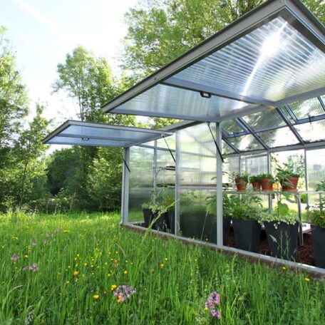 Ein Gewächshaus mit offenen Fenstern steht inmitten einer blühenden Sommerwiese. de HANSEL.kraus metalltechnik gmbh