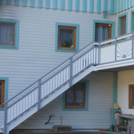 Außentreppe führt an blauer Hausfassade mit mehreren Fenstern im Innenhof entlang. HANSEL.kraus metalltechnik gmbh