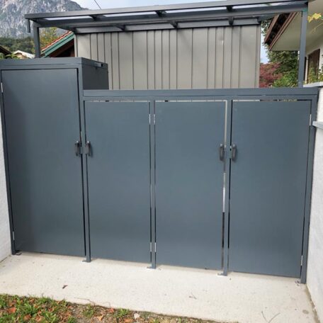 Dunkelgraue Mülltonnenbox aus Metall mit Überdachung vor einem Gartenhaus. HANSEL.kraus metalltechnik gmbh
