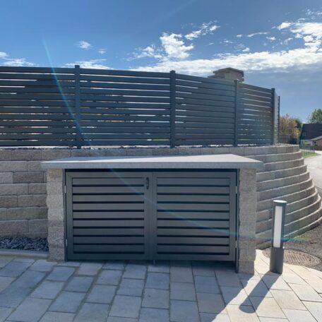 Doppelter Mülltonnen-Unterstand aus Metall vor Steinmauer mit modernem Sichtschutz und Gehweg. HANSEL.kraus metalltechnik gmbh