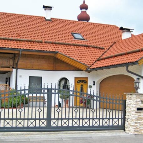 Ein Einfamilienhaus mit rotem Dach, Vorgarten, Zaun und angrenzender Garage bei Tageslicht. HANSEL.kraus metalltechnik gmbh