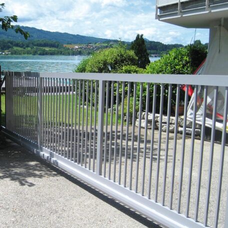Silbernes Schiebetor aus Metall vor einem modernen Haus mit Blick auf See und Berge. HANSEL.kraus metalltechnik gmbh
