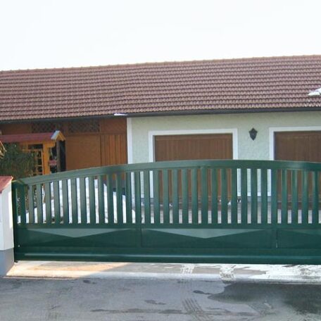 Zweiflügeliges grünes Hoftor vor Einfamilienhaus mit Doppelgarage und braunem Satteldach. HANSEL.kraus metalltechnik gmbh