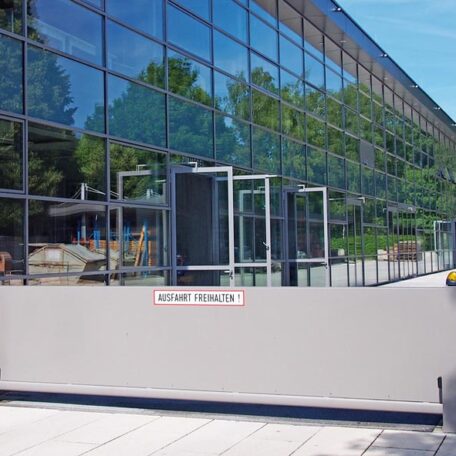 Moderne Glasfassade mit reflektierenden Fenstern, davor ein geschlossenes Zufahrtstor am Firmengebäude. HANSEL.kraus metalltechnik gmbh