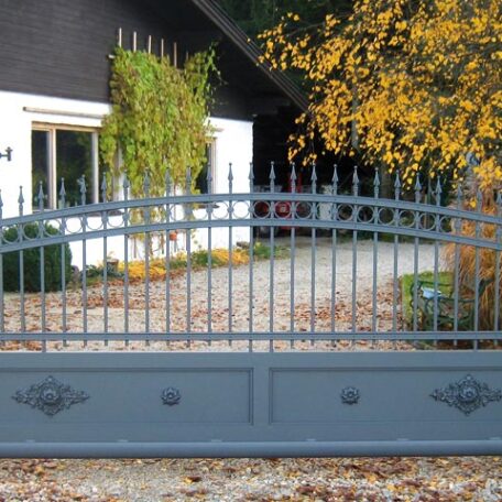 Einfahrtstor aus Metall vor einem weißen Haus mit Garten und herbstlichen Bäumen. HANSEL.kraus metalltechnik gmbh