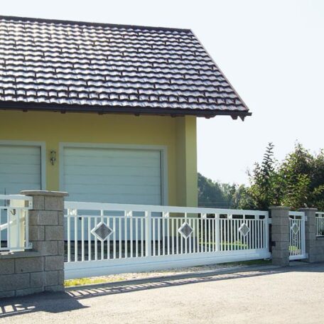 Zweiflügeliges Einfahrtstor aus Metall vor Doppelgarage und gelbem Wohnhaus, sonniger Tag. HANSEL.kraus metalltechnik gmbh
