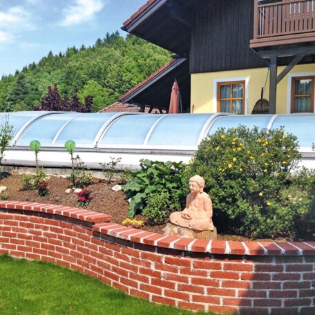 Ein Hochbeet aus Backstein mit Buddha-Figur vor einem Haus und überdachtem Pool. HANSEL.kraus metalltechnik gmbh